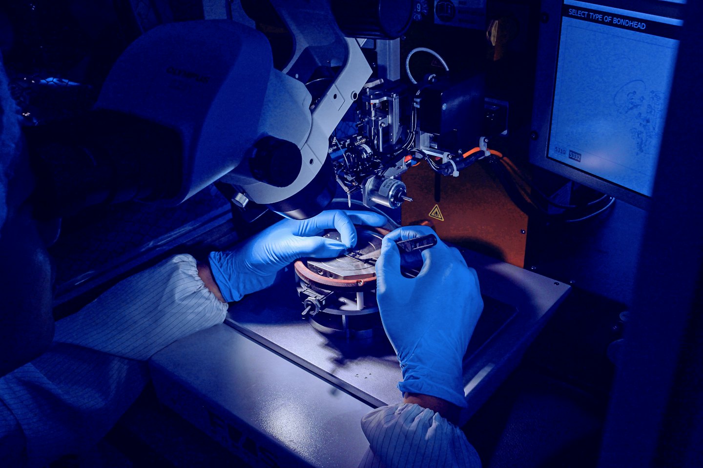 Technician in cleanroom suit works on electronic components.